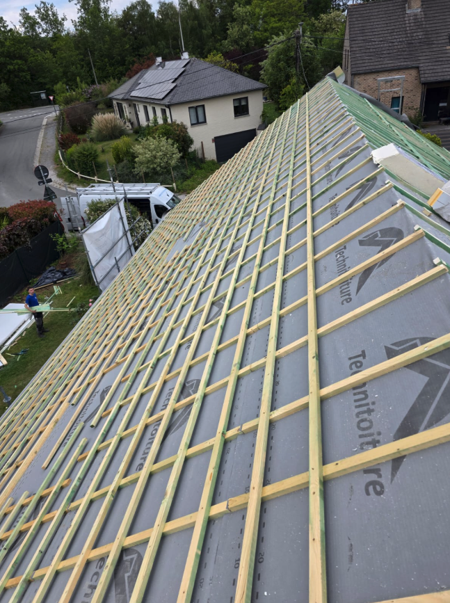 Une toiture en chantier est recouverte d’une membrane grise et de lattes en bois.